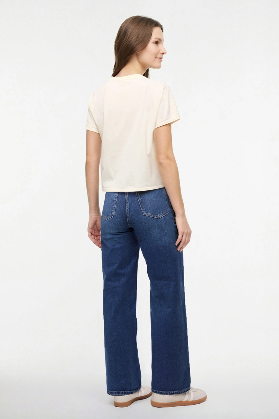 Back view of woman wearing a pale yellow t-shirt with a small chest graphic on a white background.