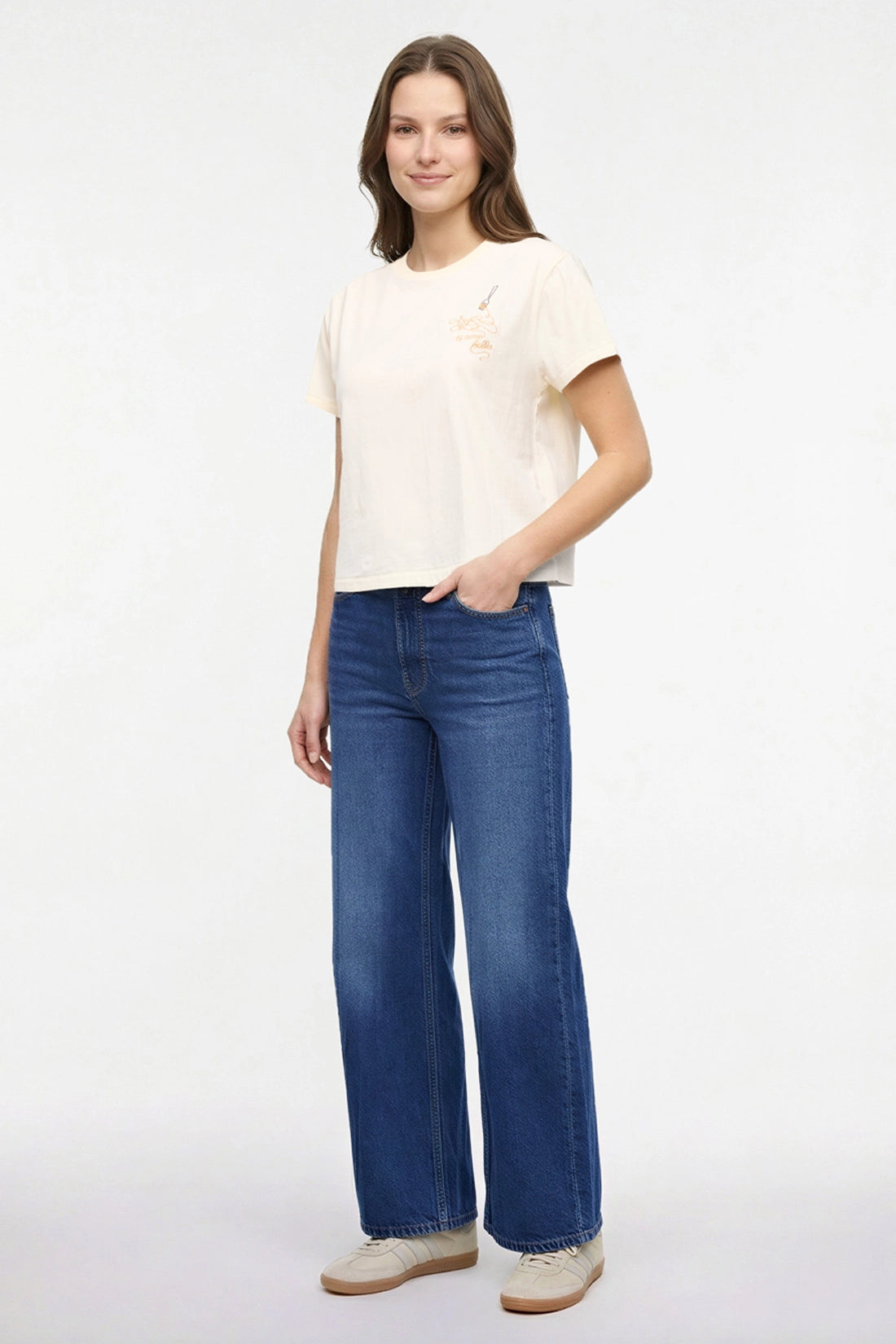 Side view of woman wearing a pale yellow t-shirt with a small chest embroidered design of spaghetti and a fork graphic on a white background.