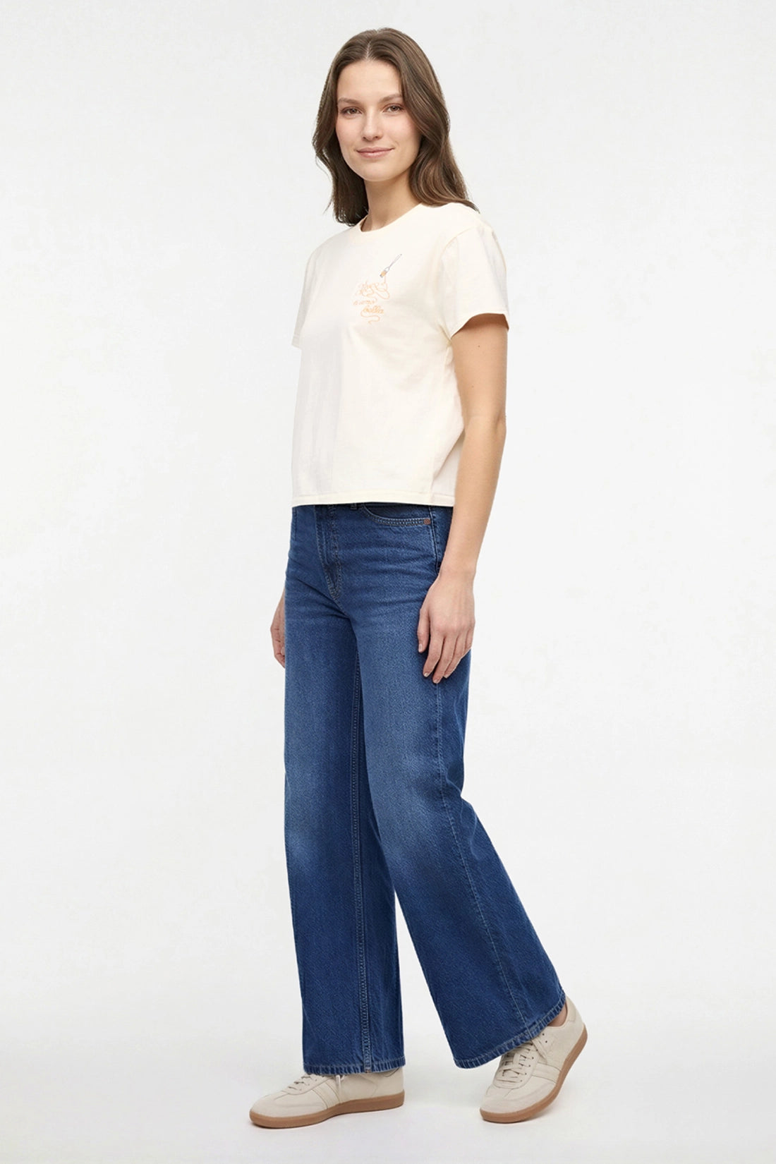 Front view of woman wearing a pale yellow t-shirt with a small chest embroidered design of spaghetti and a fork graphic on a white background.