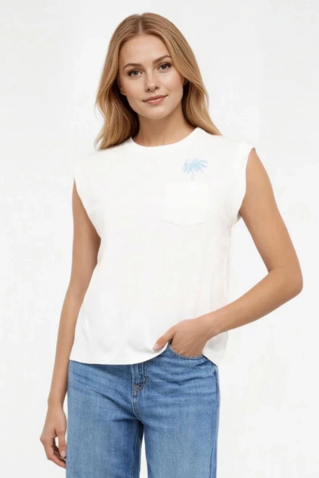 Front view of woman wearing a white t-shirt with graphic design featuring a palm tree on top left chest and blue jeans on a white background.