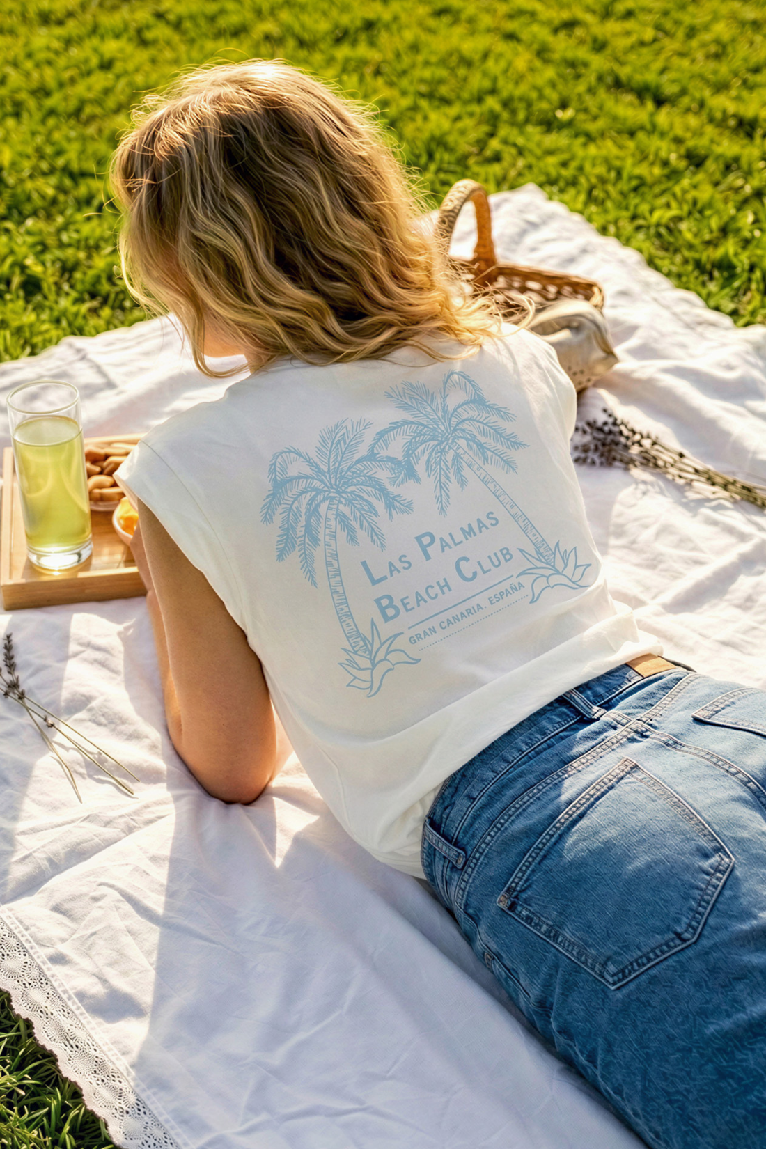 Back view of woman sitting on a blanket with a drink and tray, wearing a &