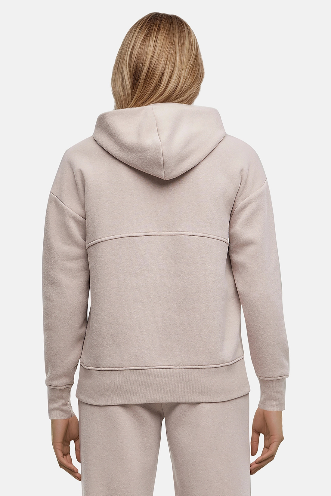 Back of woman wearing a beige hoodie and pants on a light gray background