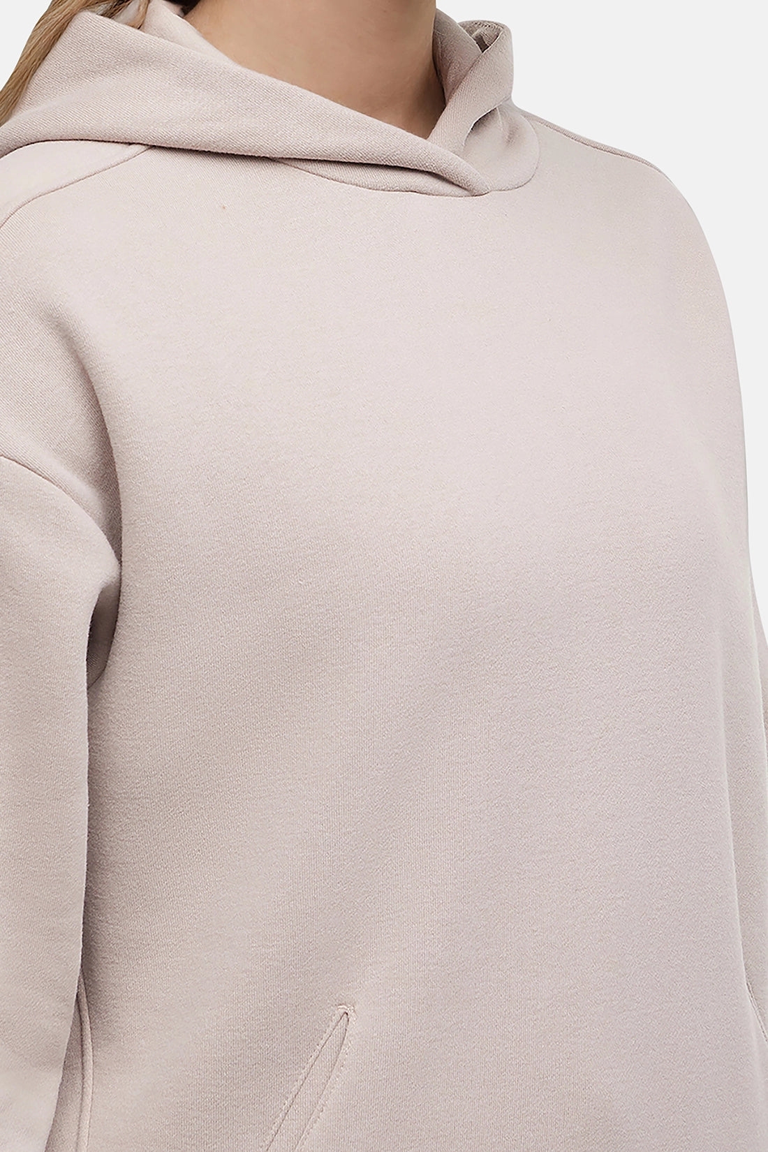 Close-up of a woman wearing a beige hoodie on a plain background