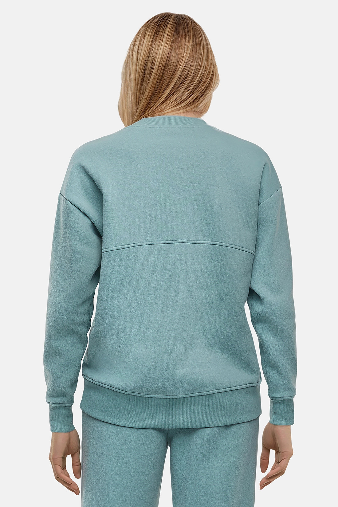 Back of woman wearing a light teal sweatshirt and pants on a white background