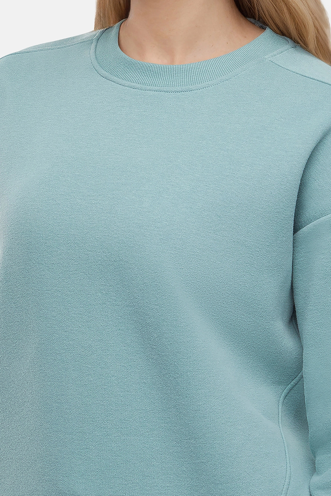 Woman wearing a light teal sweatshirt and pants on a white background