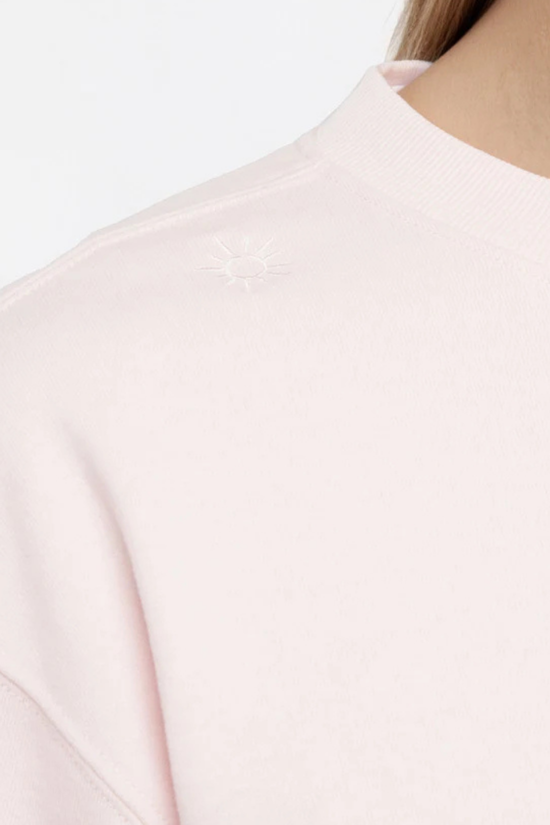 Close up front view of woman wearing a light pink sweatshirt with white sun tree on right shoulder on a white background.