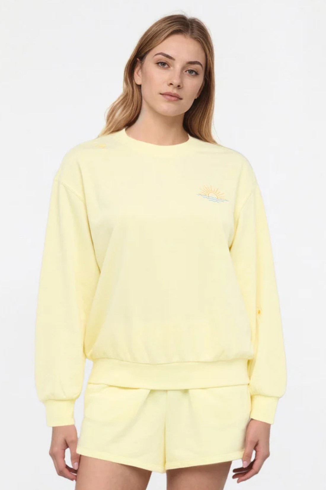 Front view of woman wearing a yellow sweatshirt and shorts on a light gray background.