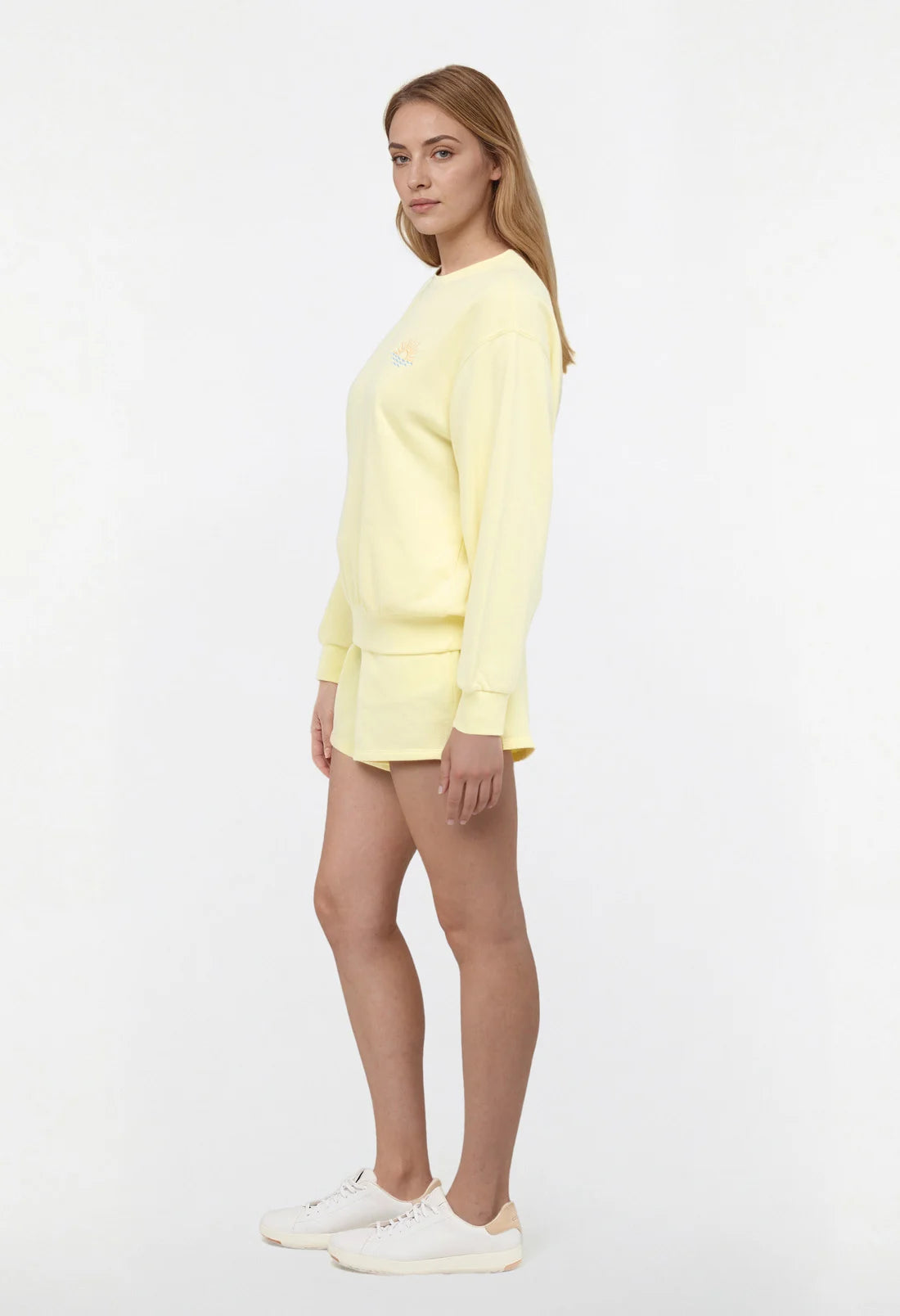 Side view of woman wearing a yellow sweatshirt and shorts on a light gray background.
