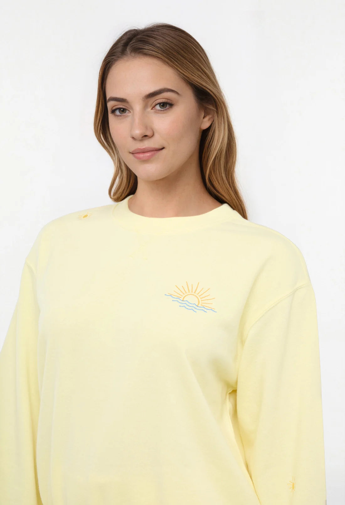 Close up view of woman wearing a yellow sweatshirt with sunset beach graphic on a light gray background.