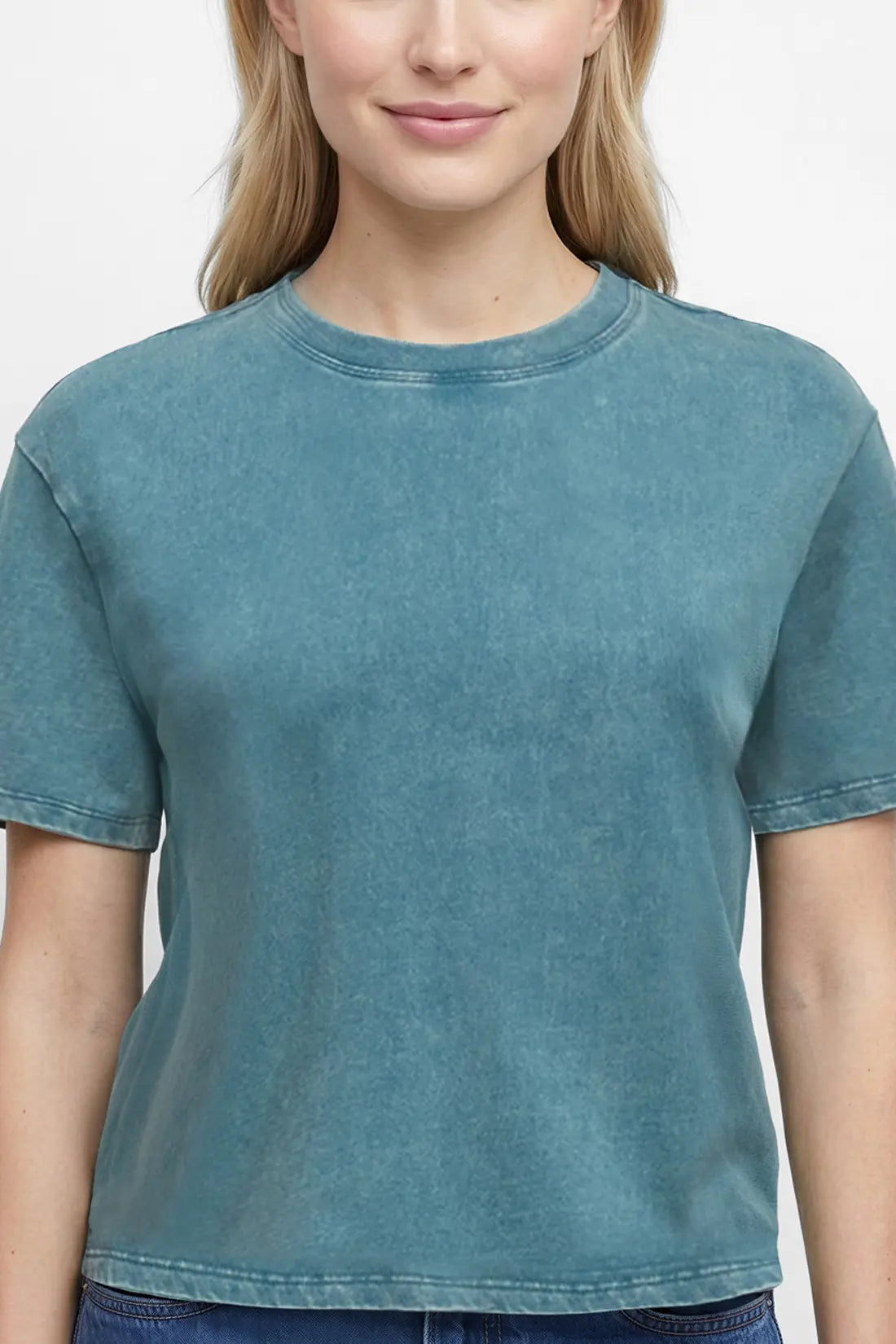 Close up front view of woman wearing a teal green t-shirt and blue jeans on a white background.