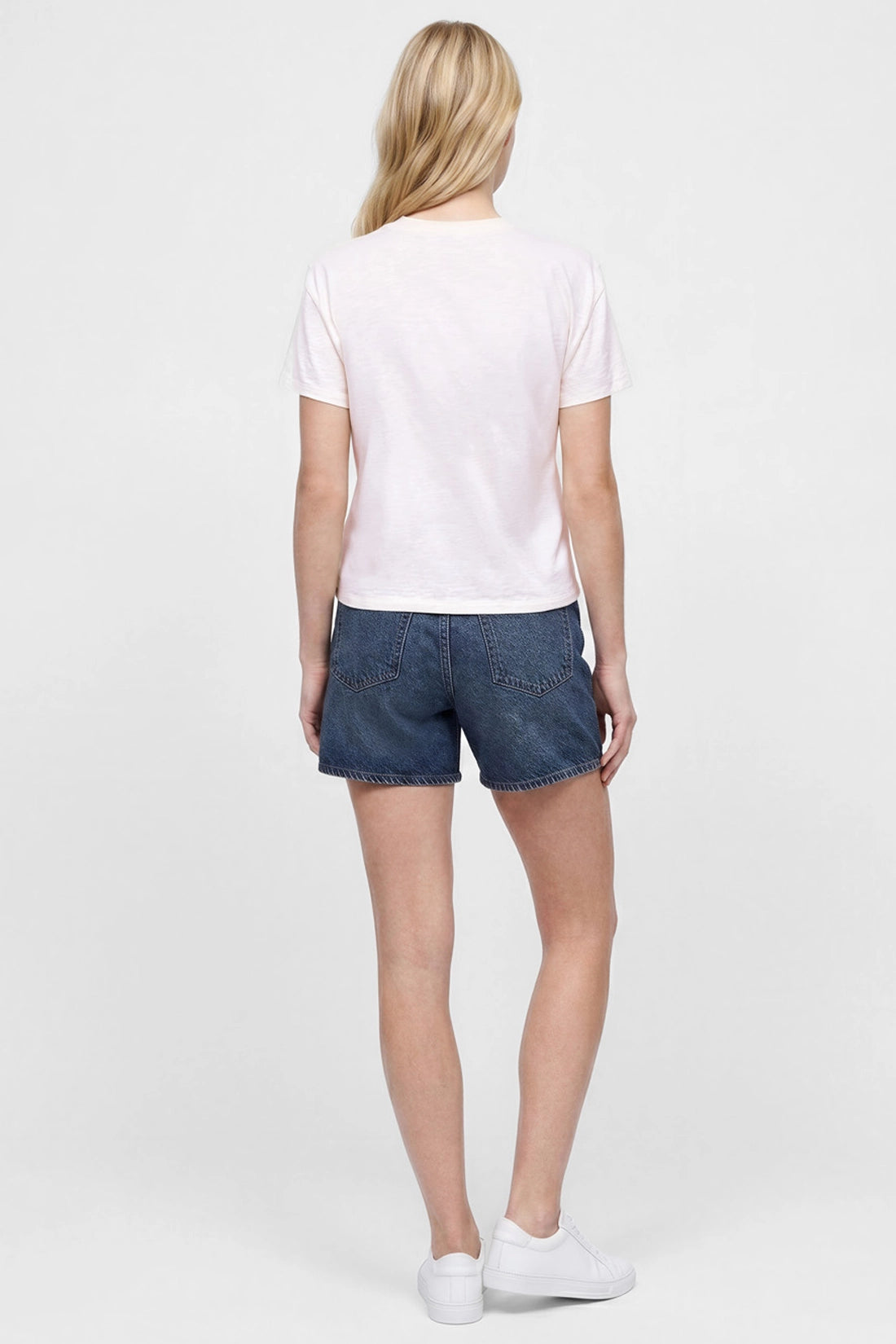 Back view of woman wearing a white t-shirt and jean shorts on a white background.