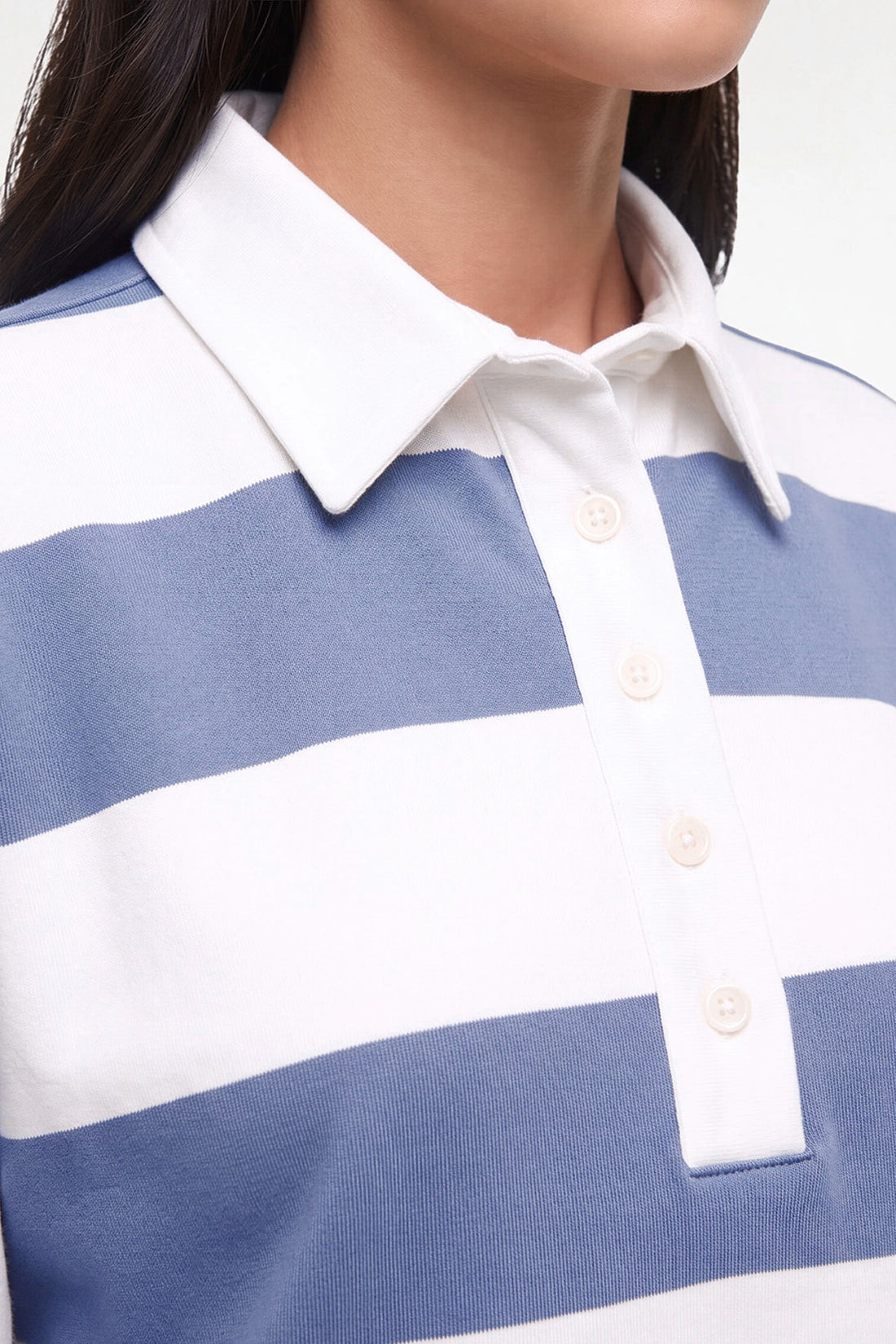 Close-up of a person wearing a blue and white horizontally striped polo shirt with a white collar and three visible buttons.