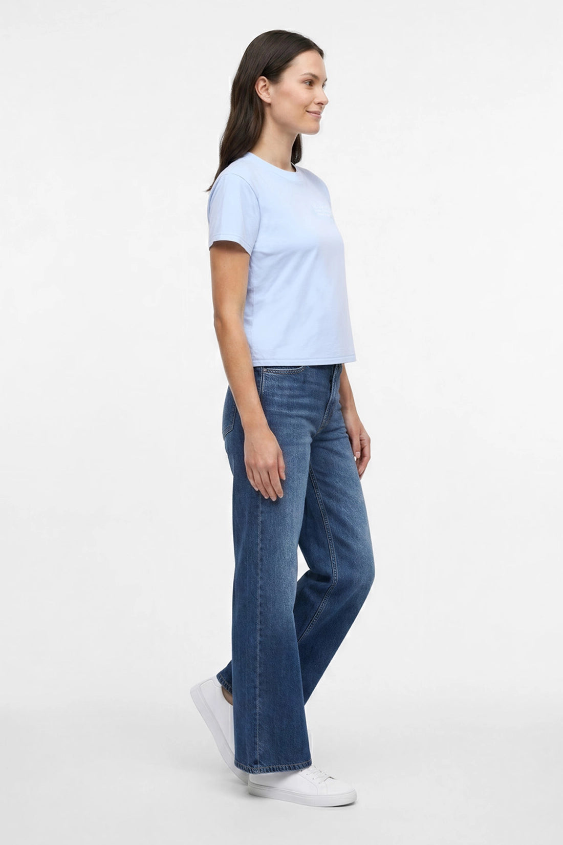 Side view of a woman wearing light blue t-shirt with embroidered &
