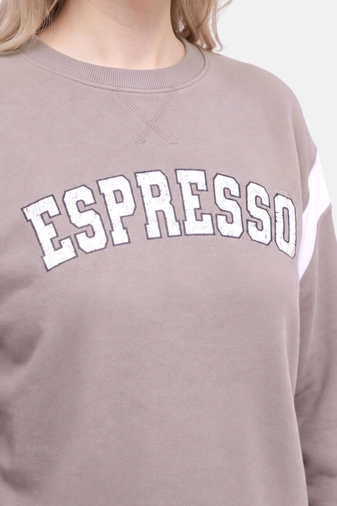 A close-up of a person wearing a taupe crewneck sweatshirt with &