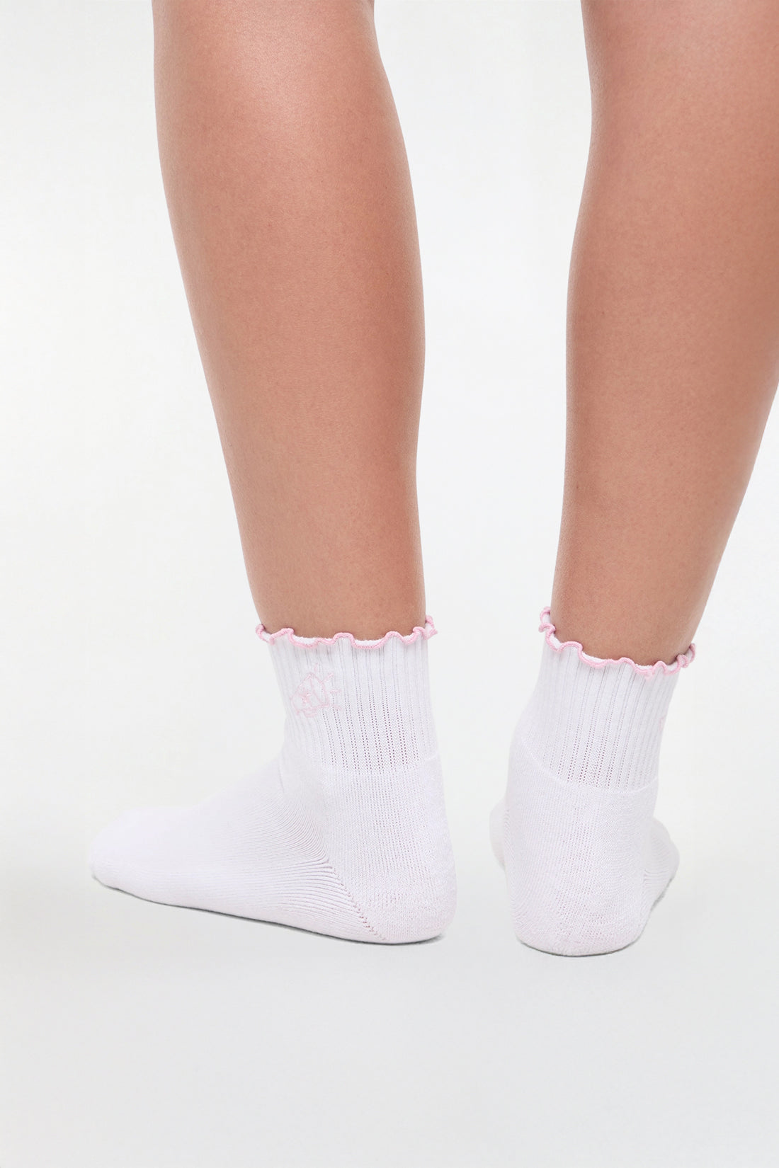 Back view of white socks with lilac ruffled trim and cheer megaphone graphic worn by a woman on a light background.