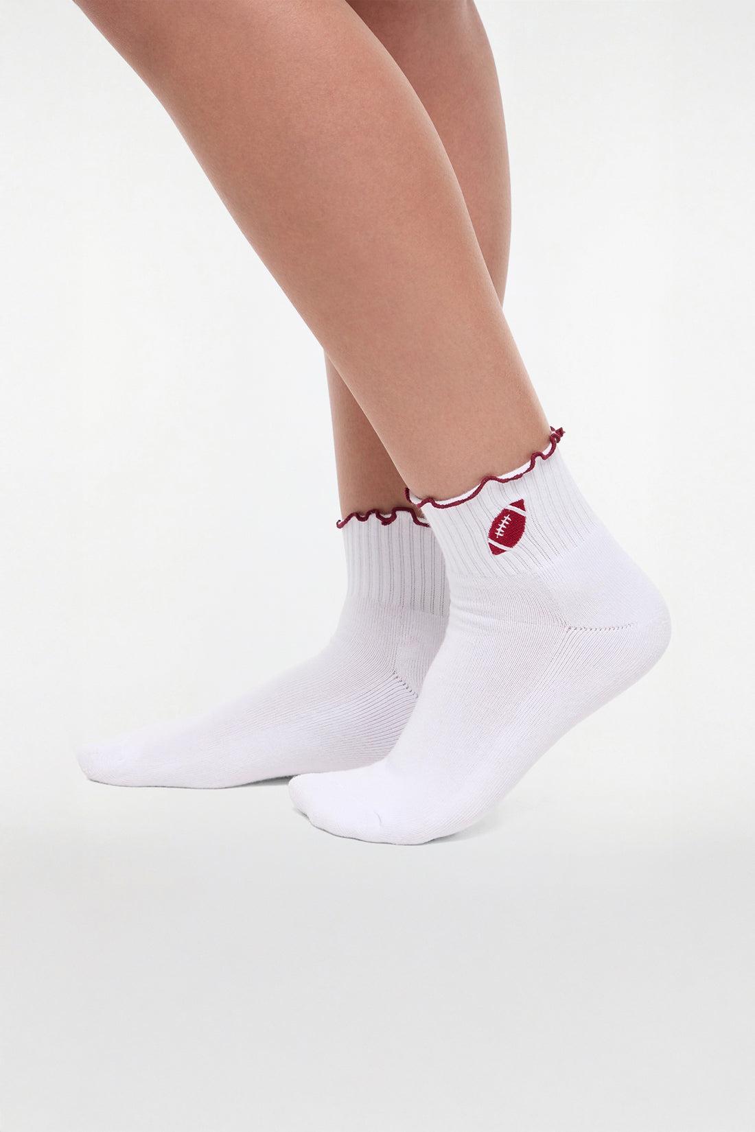 Side view of white socks with red trim and a football graphic worn by a woman on a light background.