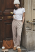Woman in casual white t-shirt and beige tapered leg pants outfit holding a coffee cup, standing in front of a wooden door.