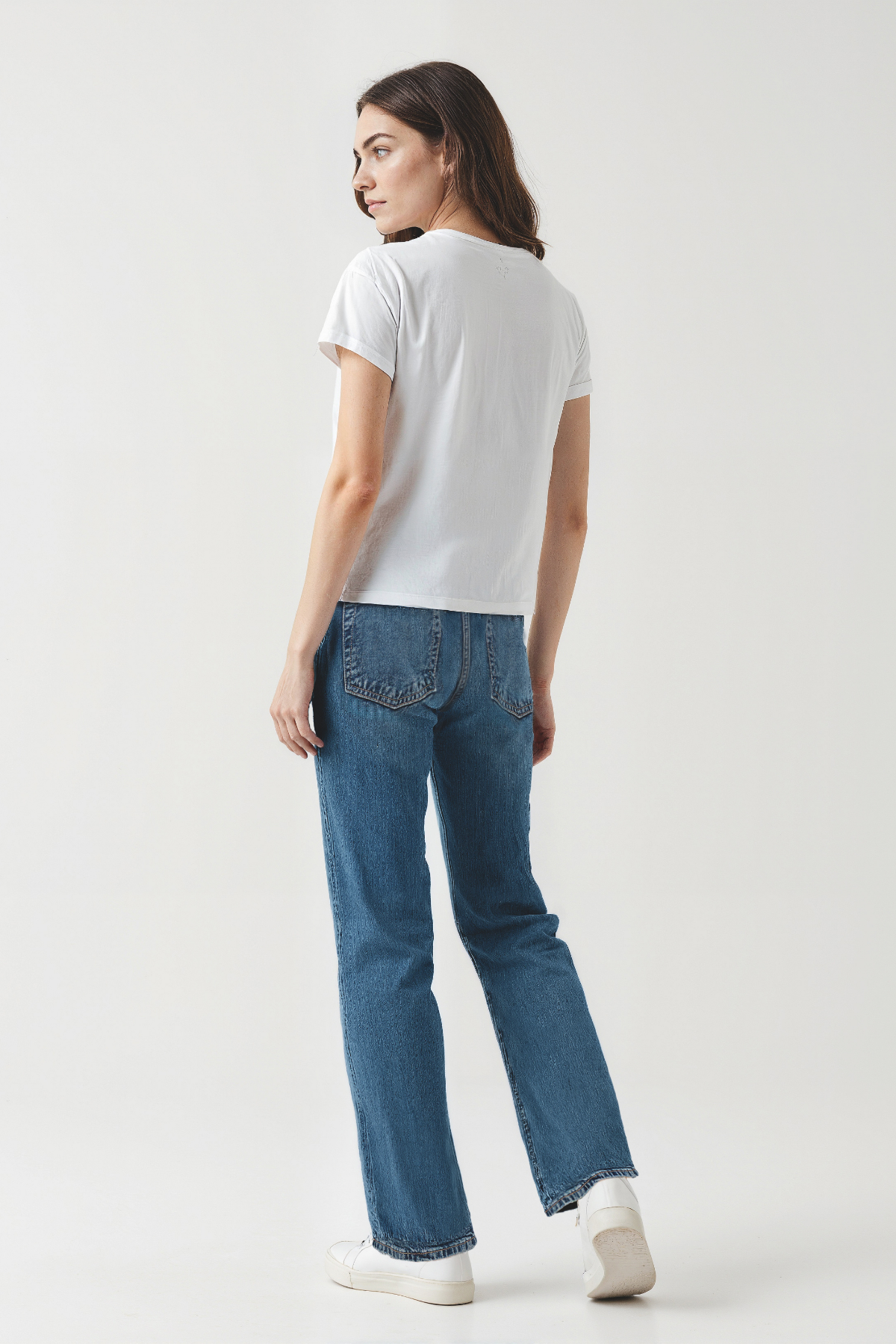 Woman wearing a white t-shirt and blue jeans on a plain background
