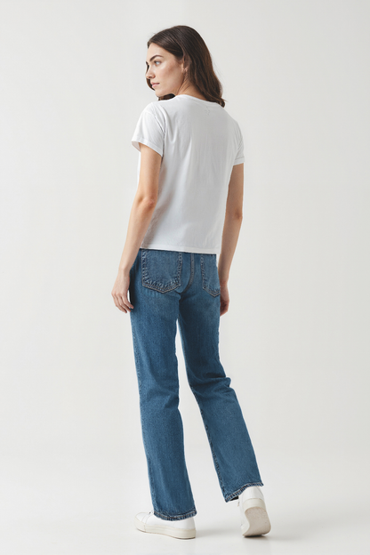 Woman wearing a white t-shirt and blue jeans on a plain background