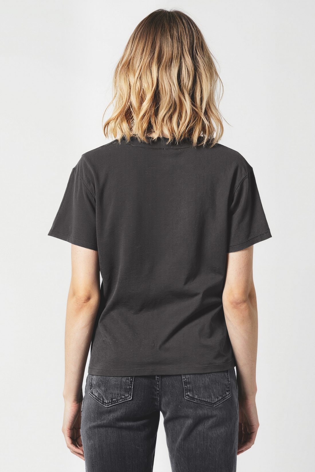 Woman wearing a black t-shirt and dark jeans on a white background