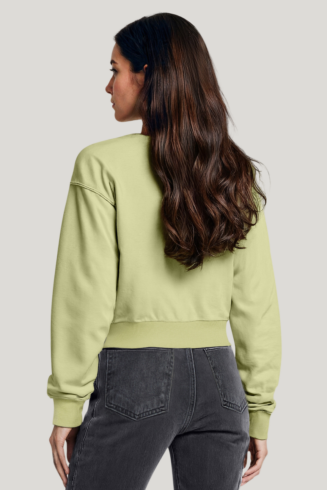 Woman wearing a light green sweatshirt and dark jeans on a white background