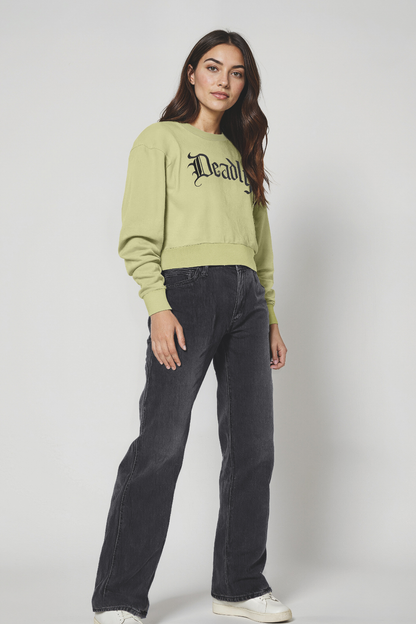 Woman wearing a light green sweatshirt with text and dark jeans on a white background