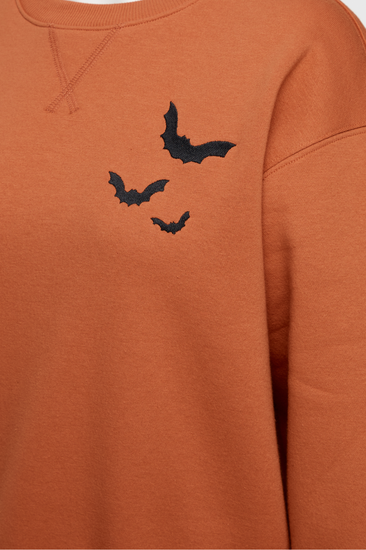 Close up of orange sweatshirt with three black bat designs on a plain background
