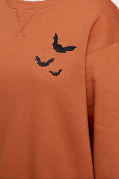 Close up of orange sweatshirt with three black bat designs on a plain background