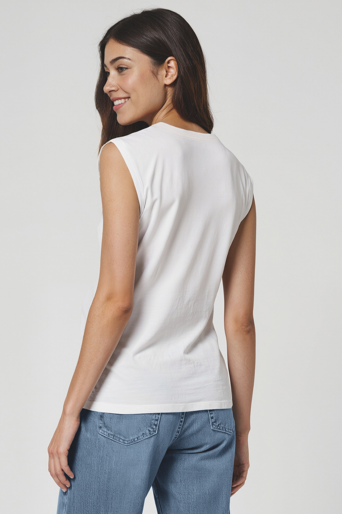 Woman wearing a white sleeveless top and blue jeans on a plain background