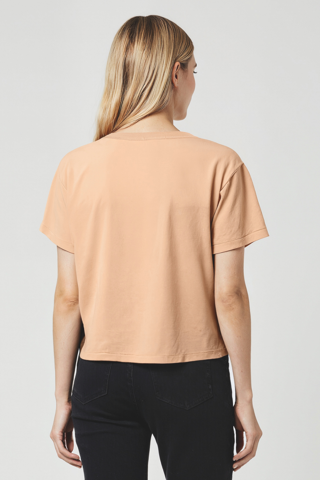 Woman wearing a tan orange t-shirt and black pants on a plain background