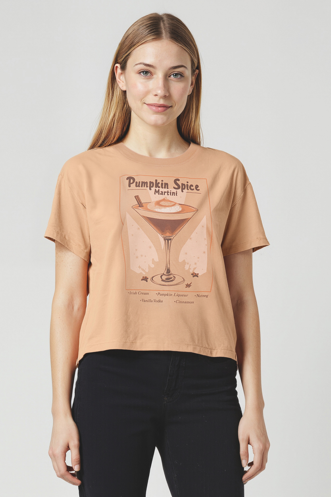 Woman wearing a tan t-shirt with a &quot;Pumpkin Spice Martini&quot; text and pumpkin spice martini graphic on a plain background