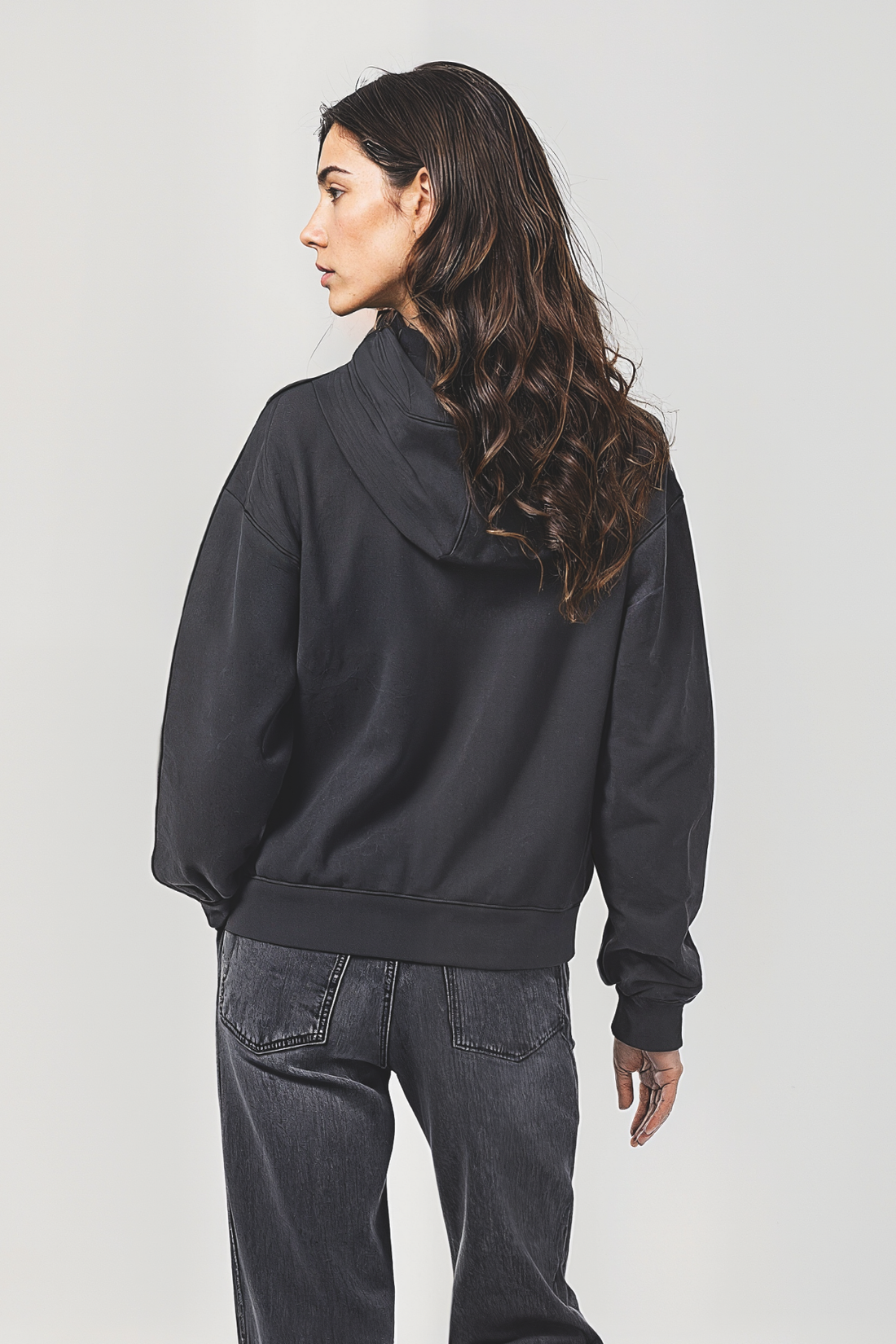 Back of woman wearing a black hoodie and jeans on a plain background