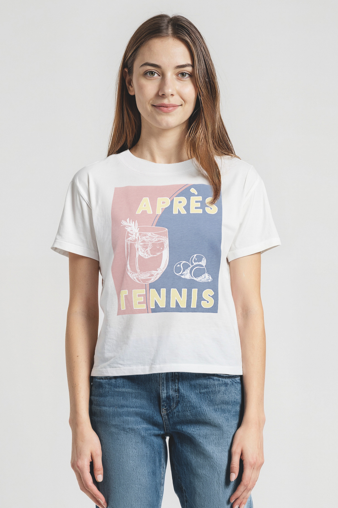 Woman wearing a white t-shirt with colorful cocktail and tennis balls graphic design and &quot;APRES TENNIS&quot; text on a plain background