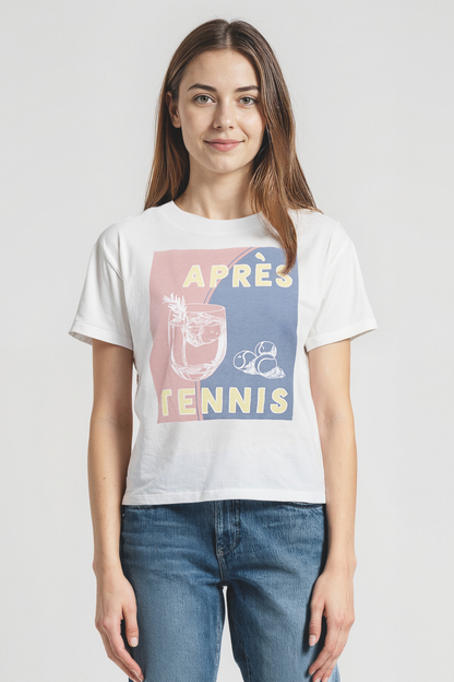 Woman wearing a white t-shirt with colorful cocktail and tennis balls graphic design and &quot;APRES TENNIS&quot; text on a plain background
