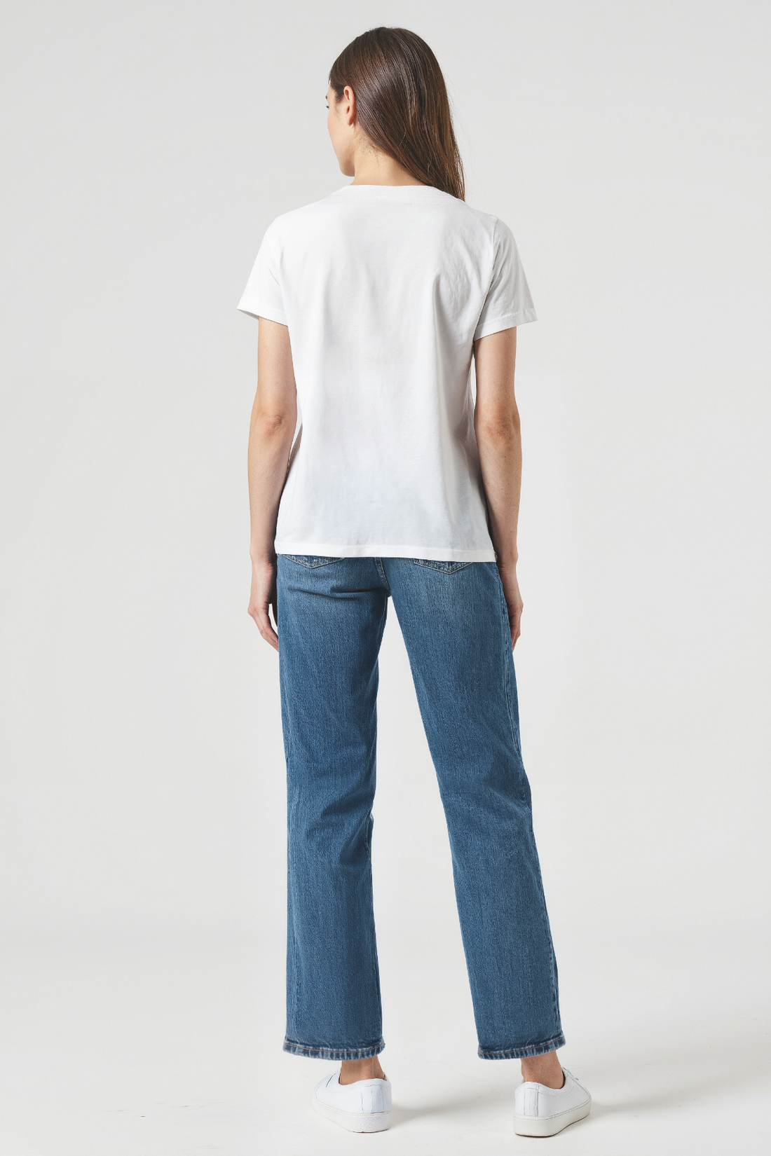 Back view of a woman wearing a white t-shirt and blue jeans on a plain background