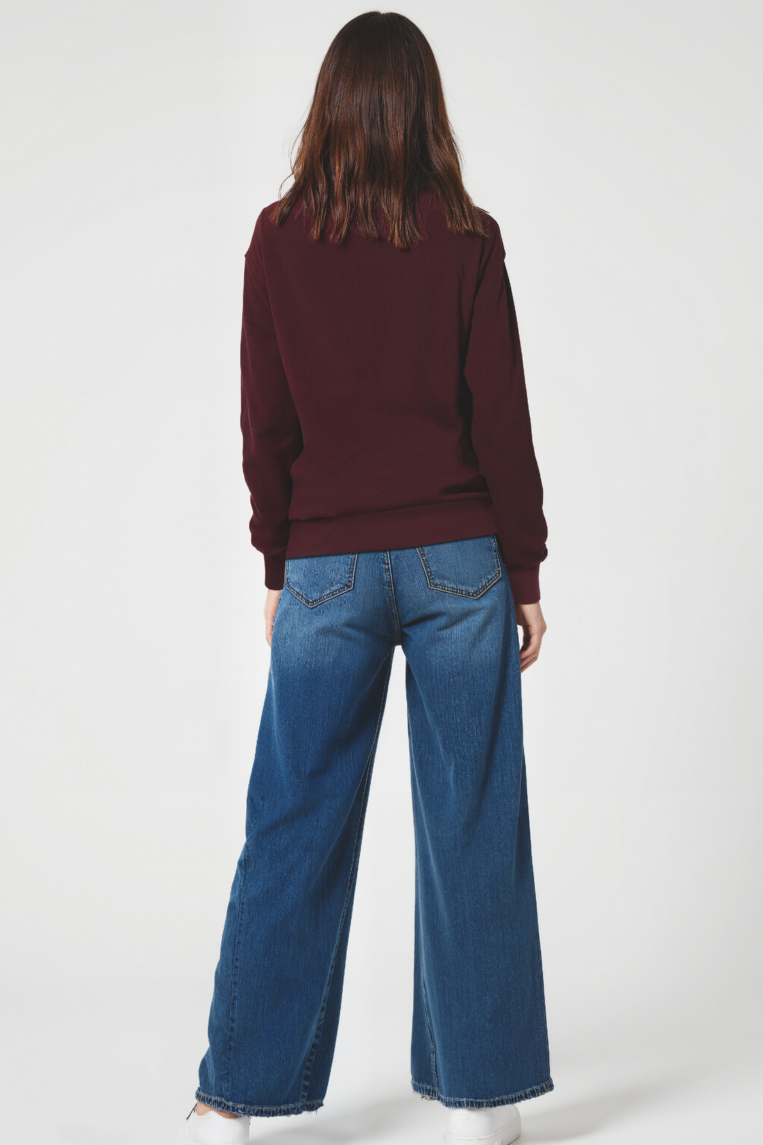 Woman wearing a maroon sweatshirt and blue jeans on a white background
