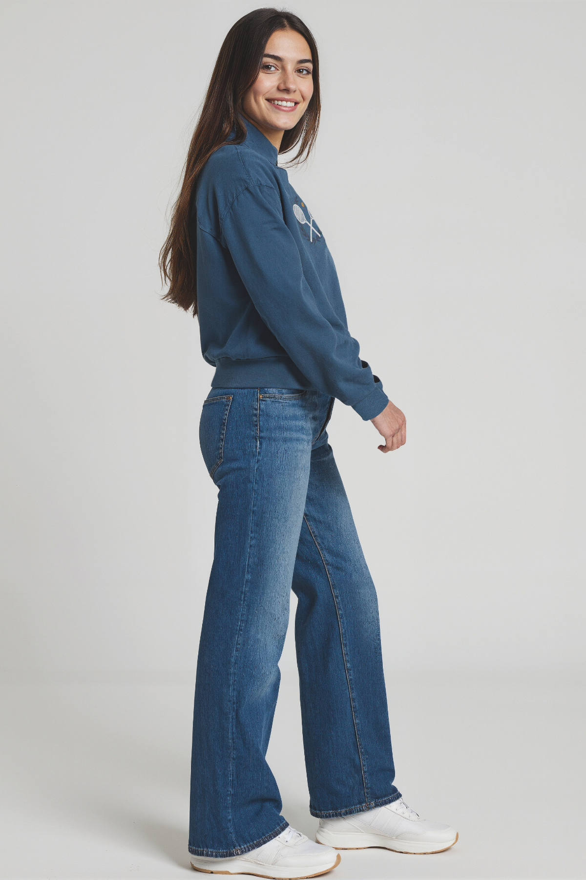 Woman wearing a blue 1/2 zip sweatshirt and jeans on a white background