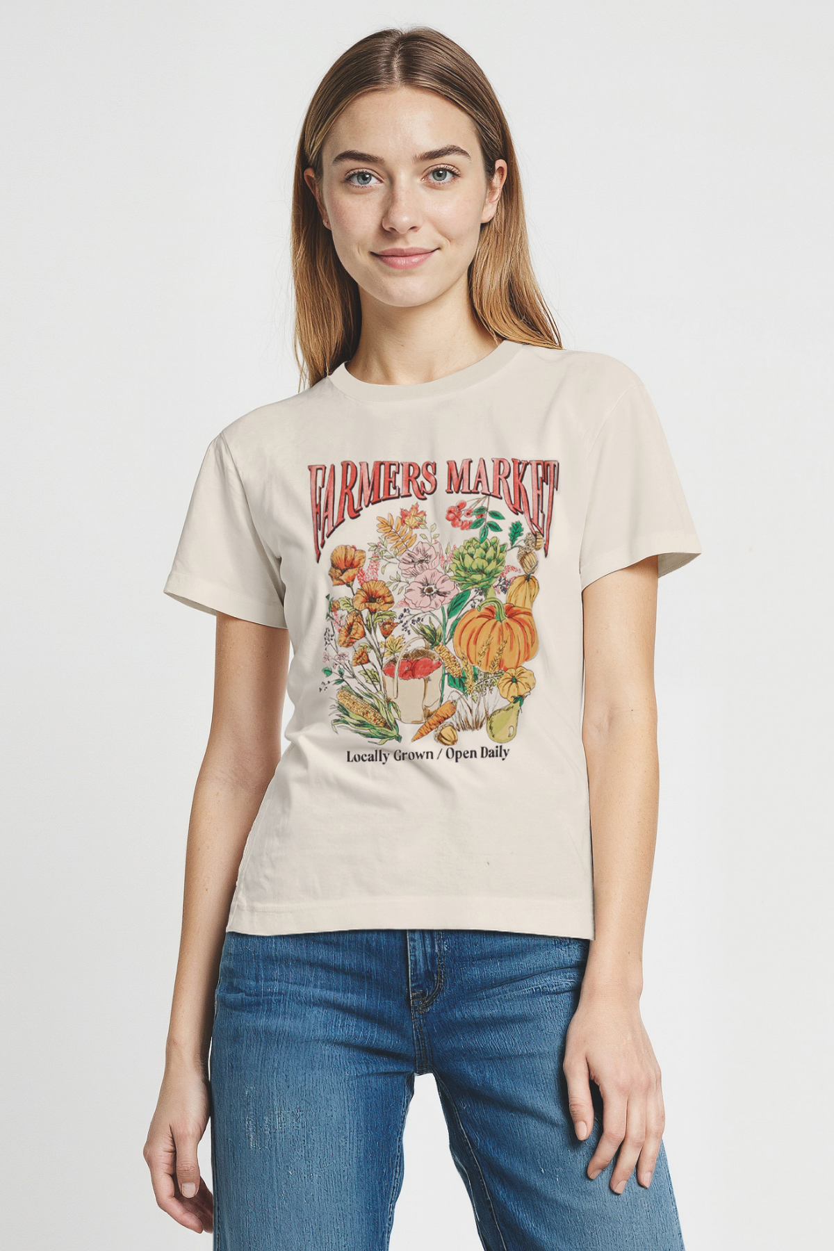 Woman wearing a beige t-shirt with a colorful graphic design of &quot;FARMERS MARKET; Locally Grown / Open Daily&quot; text on a plain background