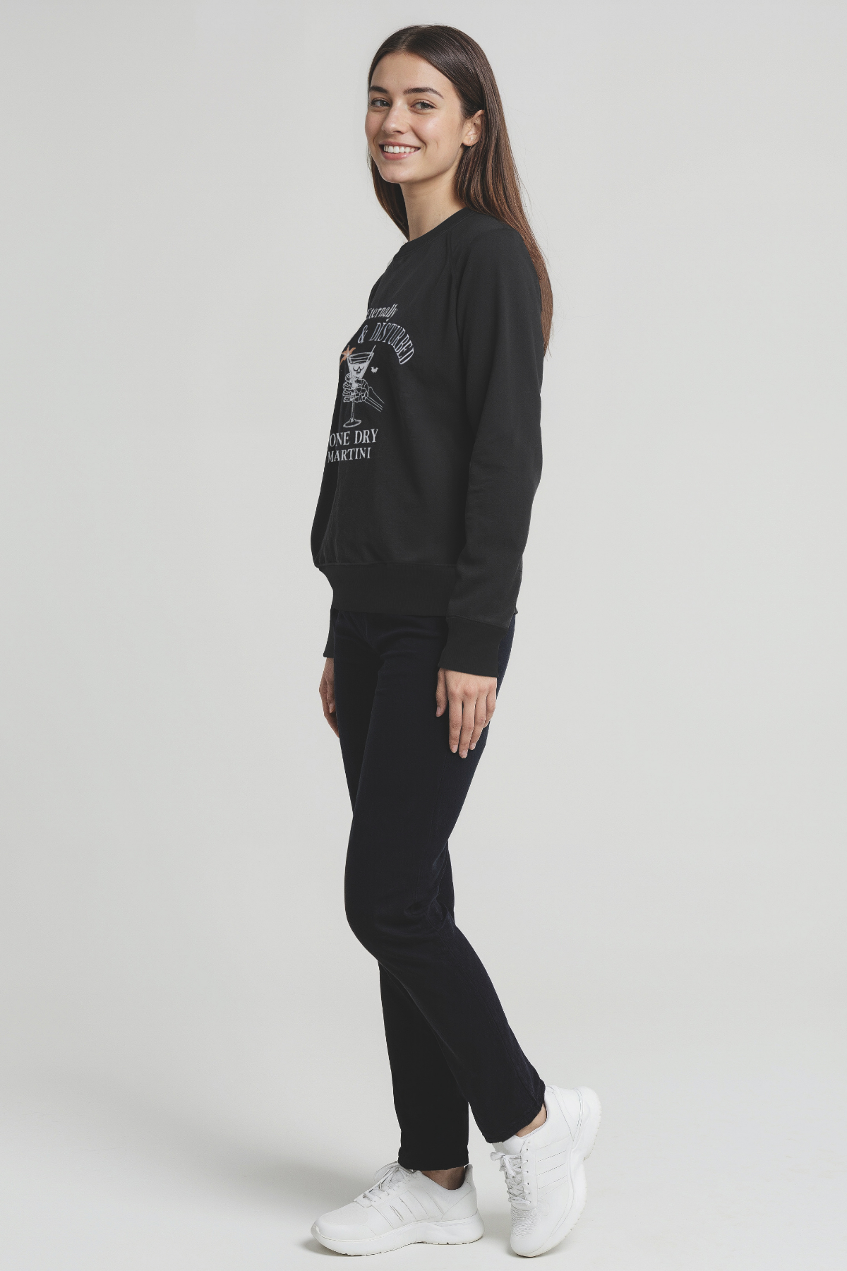 Woman wearing a black sweatshirt and pants with white sneakers on a light gray background