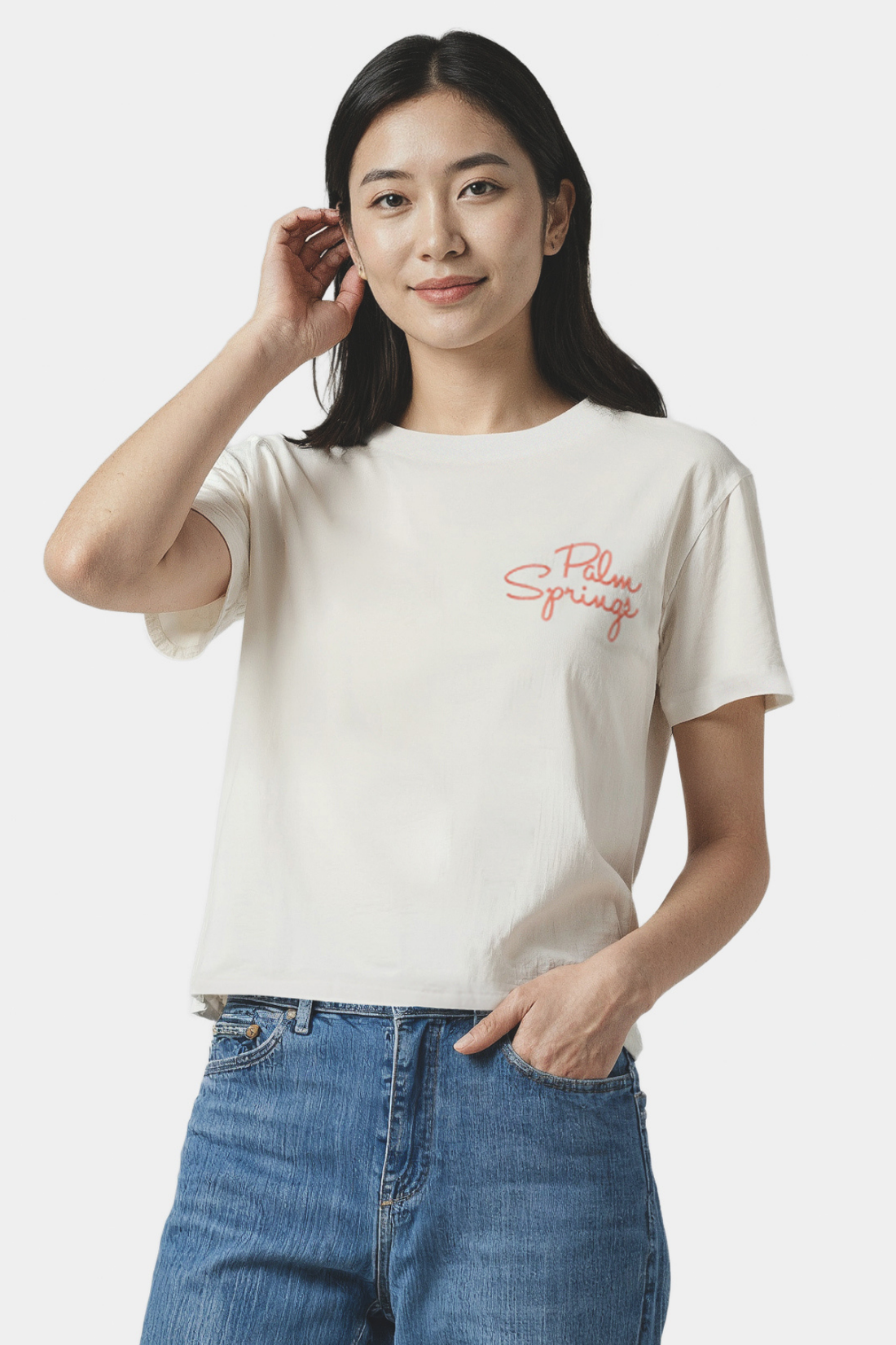 Woman wearing a white t-shirt with a red &quot;Palm Springs&quot; text and blue jeans on a white background