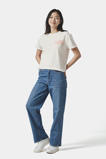 Woman wearing a white t-shirt with a &quot;Palm Springs&quot; text and blue jeans on a white background