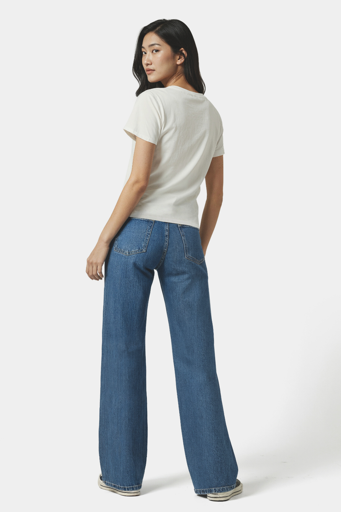 Backside view of a woman wearing a white t-shirt and blue jeans on a white background