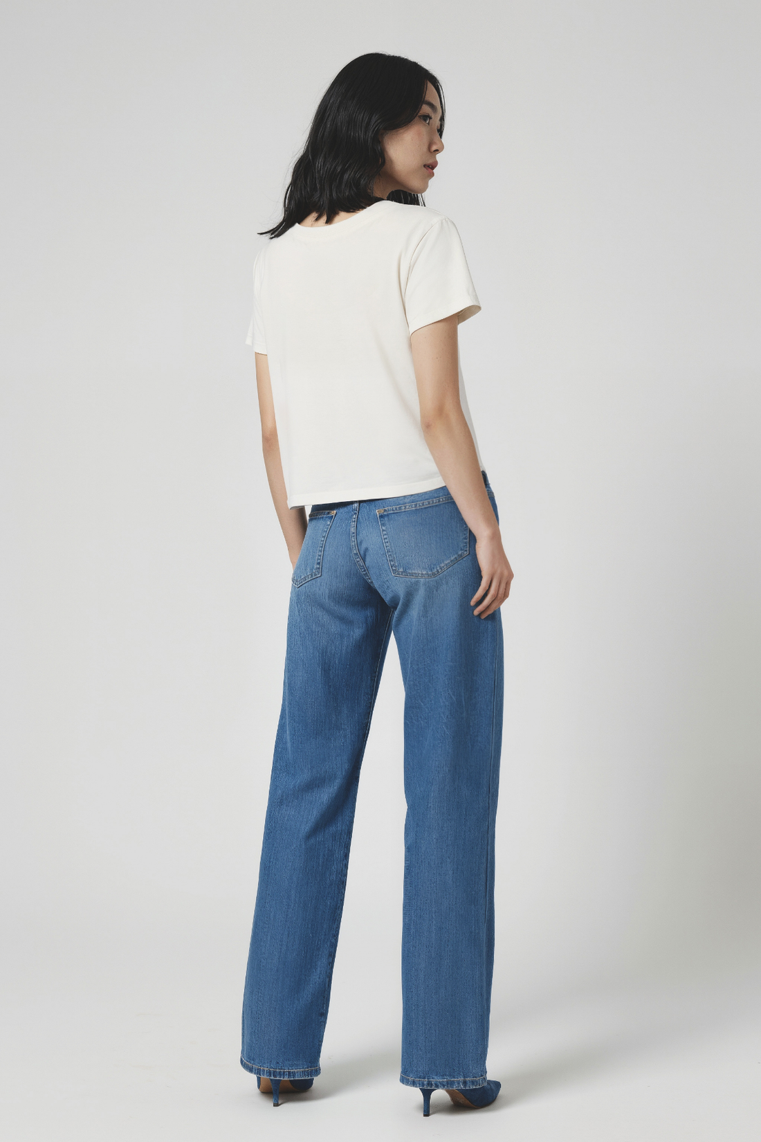 Woman wearing a white t-shirt and blue jeans on a plain background