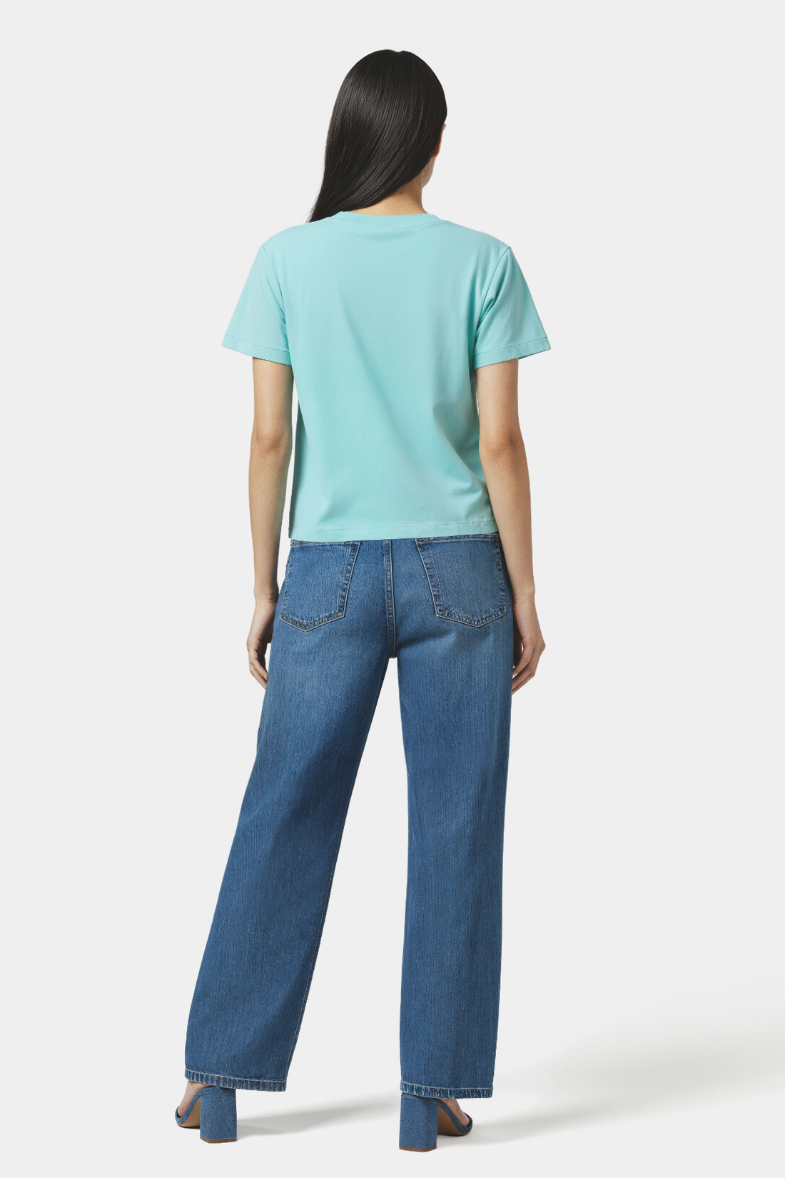 Back of woman wearing a light blue t-shirt and blue jeans on a white background