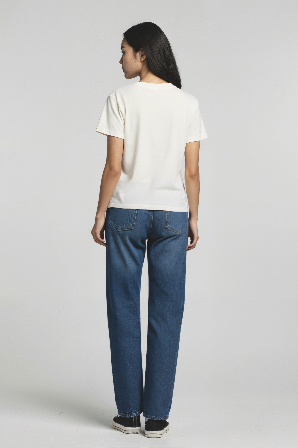 Back of woman wearing a white t-shirt and blue jeans on a plain background