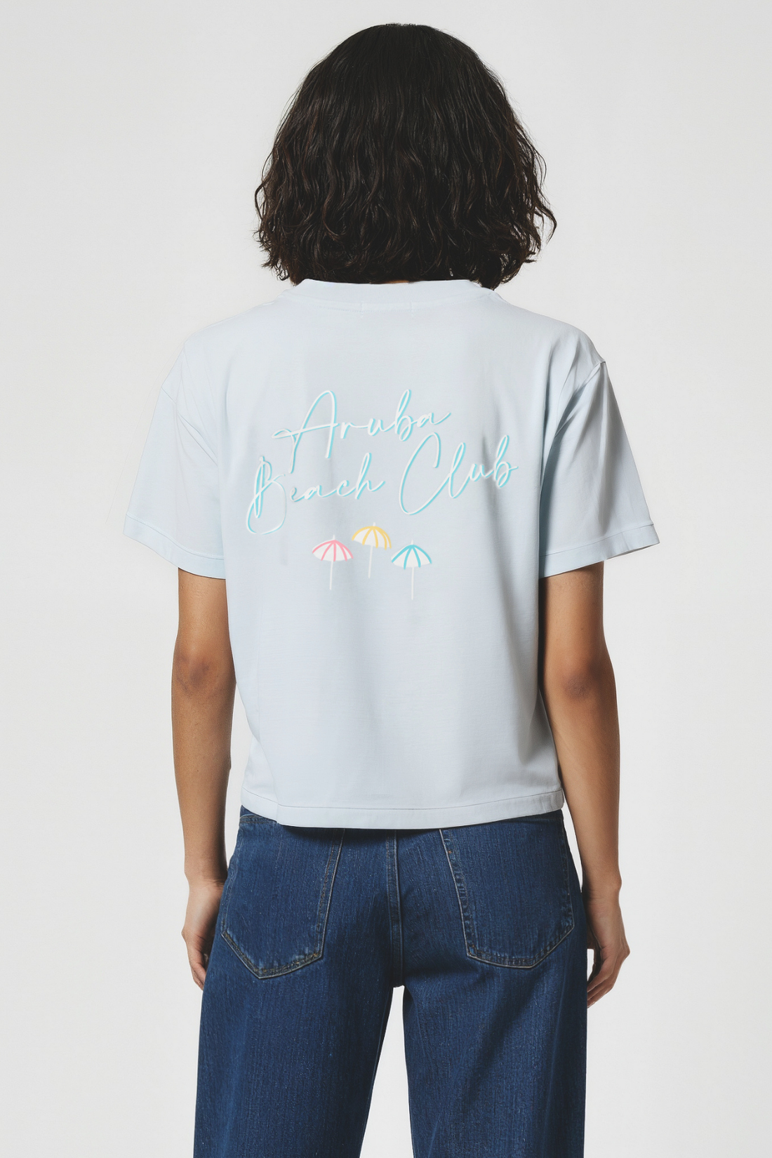 Woman wearing a light blue t-shirt with colorful text and graphics on the back, standing against a plain background.