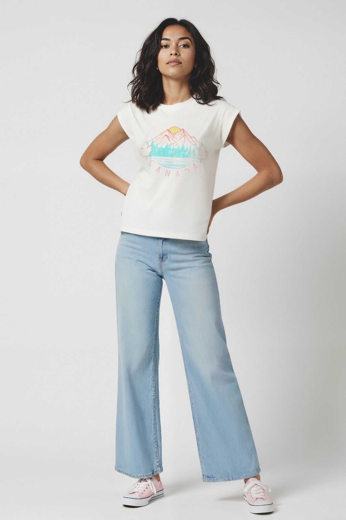 Woman wearing a white t-shirt with a colorful mountain, trees, and sun graphic design and &