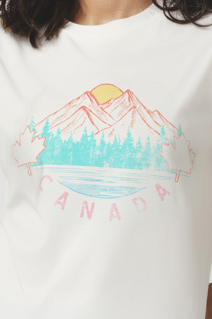 Woman wearing a white t-shirt with a colorful mountain, trees, and sun graphic design and &
