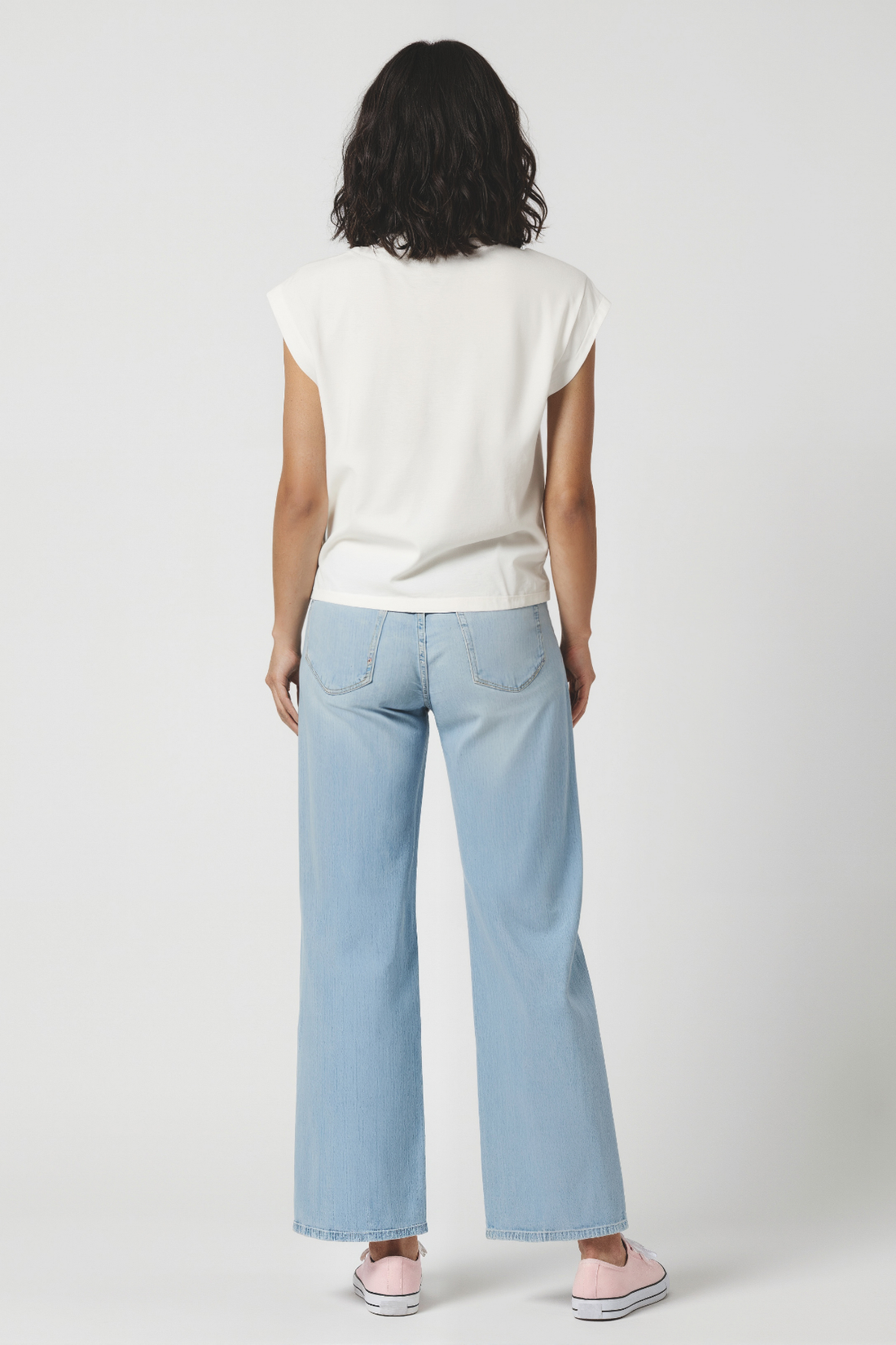 Back view of woman wearing a white t-shirt and light blue jeans on a plain background