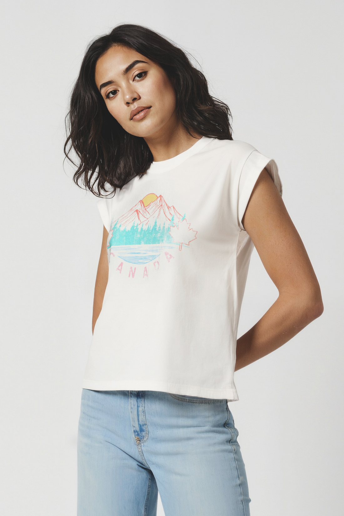Woman wearing a white t-shirt with a colorful mountain, trees, and sun graphic design and &